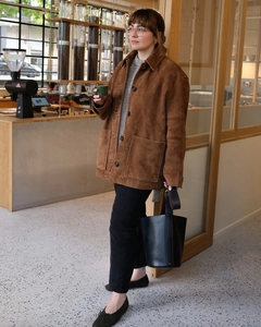 Détail d'une veste vintage en daim marron avec un sac seau en cuir noir dans un café