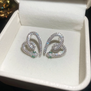 Macro shot of silver snake-shaped heart earrings with cubic zirconia and green gem eyes