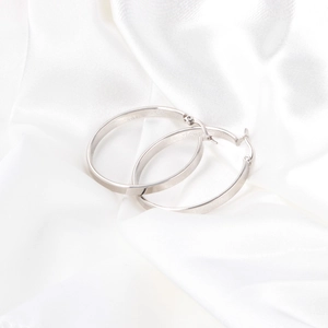 Detail of silver brushed stainless steel hoop earrings on white silk fabric background