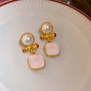 Dettaglio di orecchini vintage con pietra rosa e perla bianca su un piatto di ceramica