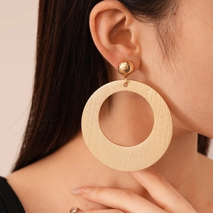 Close-up of large golden geometric hoop earrings with brushed metal texture on a model