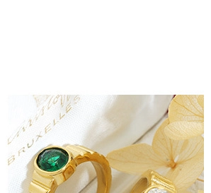 Vue macro d'une bague plaquée or 18k avec une pierre verte sur un pochon blanc
