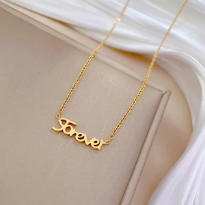 Macro detail of golden Forever cursive pendant on a minimalist titanium steel chain