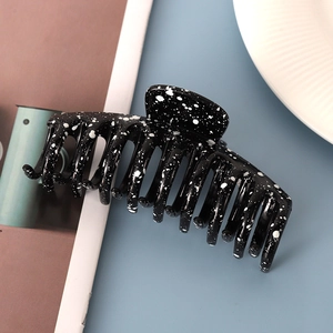 Macro detail of large black hair claw clip with white ink splash pattern and smooth resin finish