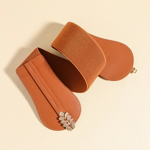 Detail view of caramel brown elastic belt with golden leaf buckle and sparkling crystals