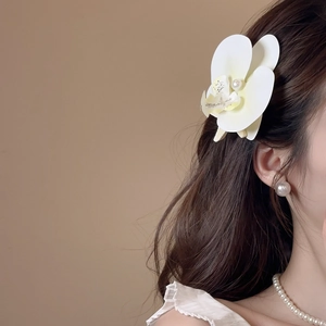 Detail view of a white orchid hair clip with pearl embellishment on a female model