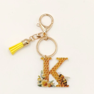 Detail of letter K acrylic keychain with honey bee pattern and yellow flower tassel