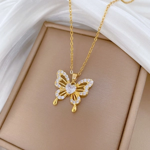 Close-up of a gold butterfly necklace with a heart zircon pendant on a beige stand