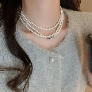 Detailansicht einer drelagigen Perlenkette mit Silberverschluss an einem grauen Cardigan