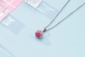 Detail of silver chain with pink and white crystal pave ball pendant on blue surface