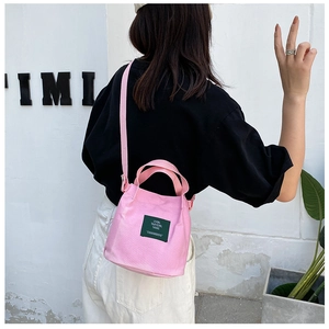 Detail view of pink canvas bucket bag featuring a green woven label and shoulder strap