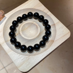 Close-up of polished black obsidian beaded bracelet on a light wood display tray