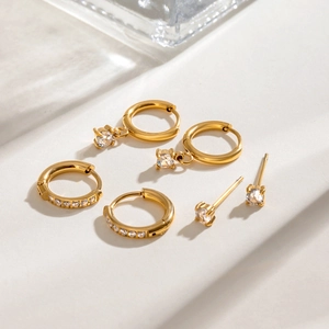 Close-up of three pairs of gold stainless steel hoop and stud earrings with crystals
