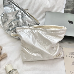 Detailed view of silver and white quilted heart makeup bags with bow patterns on soft bedding