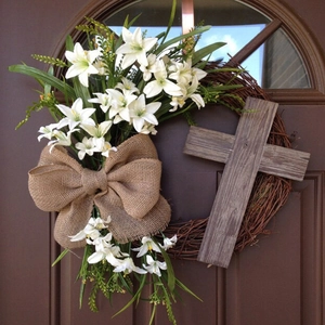 Close-up of Easter wreath with white lilies, burlap bow, and wooden cross on vine base