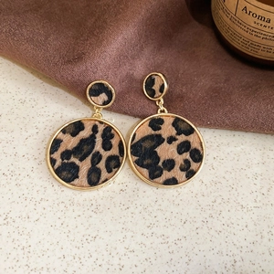 Detail of round leopard print earrings with gold frames on a vintage textured surface