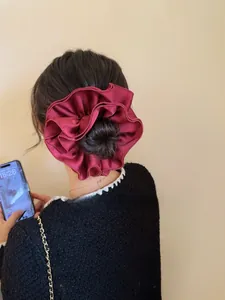 Close-up of a burgundy satin pleated scrunchie styled on a low bun hairstyle