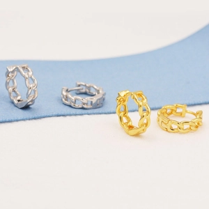 Detail of gold and silver cuban link chain hoop earrings on a blue and white background