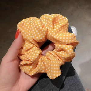 Handheld view of orange fabric scrunchie with white polka dot pattern for women hair