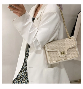 Detail of straw woven bag featuring delicate pearl trim and a golden metallic lock clasp