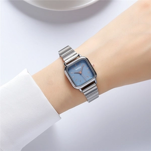 Detail of square silver steel watch with light blue dial and rose gold accents on wrist