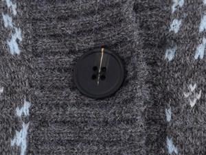 Detail of grey knitted cardigan showing blue jacquard pattern and striped black button