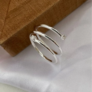 Macro shot of silver sterling three-loop spiral ring with zircon on white fabric