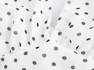 Détail du tissu en mousseline blanche à pois noirs montrant une texture plissée