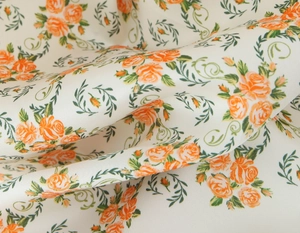 Detail of satin floral fabric featuring orange roses on a cream twill background