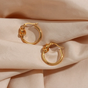 Detailed close-up of gold titanium steel knotted hoop earrings on champagne silk fabric