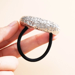 Close-up of elastic hair tie featuring a textured silver metallic ornament on beige background