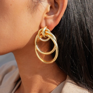 Close-up of golden triple-interlocking hoop earrings worn by a model in bright sunlight