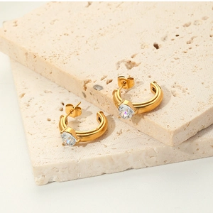 Close-up of gold C-shaped earrings with a heart-shaped crystal on stone slabs