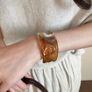 Detail view of amber acrylic bangle featuring natural marble texture and irregular surface