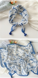 Detailed view of a white linen scarf with blue floral prints and tassel corner accents