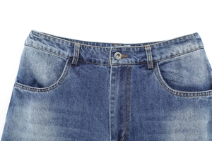 Detail of washed blue denim jeans showing the waist, metal button, and front pocket stitching