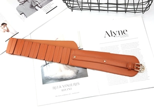 Detail of an orange-brown wide leather corset belt with gold buckle on a magazine