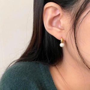 Minimalist gold hoop earrings with white round pearl pendants for women on model