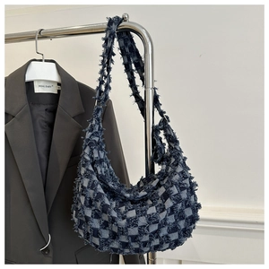 Detail of checkered denim fabric with frayed edges on a stylish crossbody shoulder bag