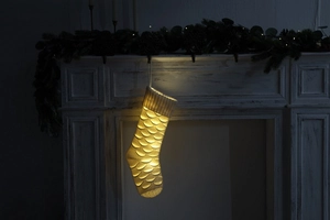 Close-up of white knitted Christmas stocking with scale pattern and warm LED lights
