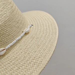 Vintage flat straw hat for women with white shell and bead decor on light grey background