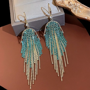 Detailed view of emerald rhinestone fringe earrings with gold tassels on leather