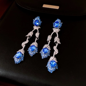 Detailed view of silver crane drop earrings with blue gems and crystals on black leather