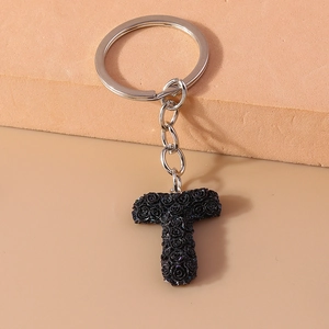 Close-up of letter T keychain featuring black rose floral textures on silver alloy metal