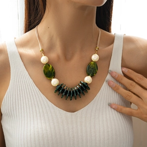 Detail of bohemian necklace featuring cream braided cord, green resin and faux pearls
