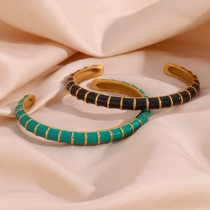 Close-up of enamel drip gold-plated open bangles in black and teal on silk fabric