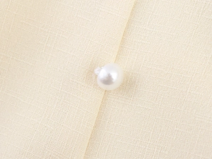 Detail of elegant beige textured fabric with a polished white pearl button closure