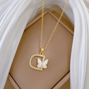 Macro shot of gold D-letter pendant with white butterfly and crystals on silk background