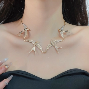 Detailaufnahme einer goldenen Schwalben-Halskette mit Flügeln getragen von einem Model
