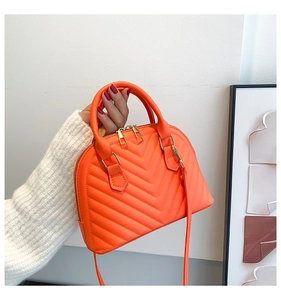 Detail of orange shell-shaped handbag with V-quilted texture and gold-tone metal zipper